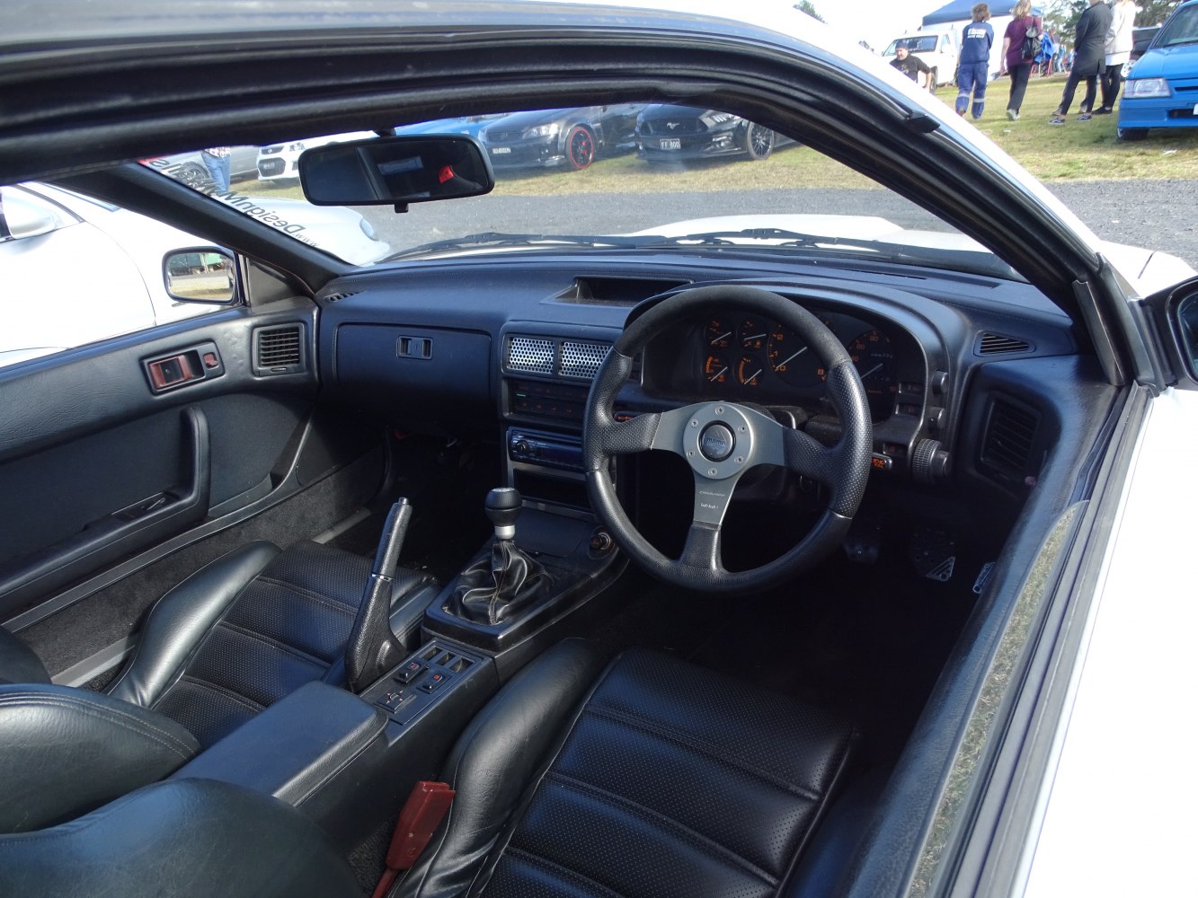 Leather steering wheel and manual transmission gear shift inside classic sports car.