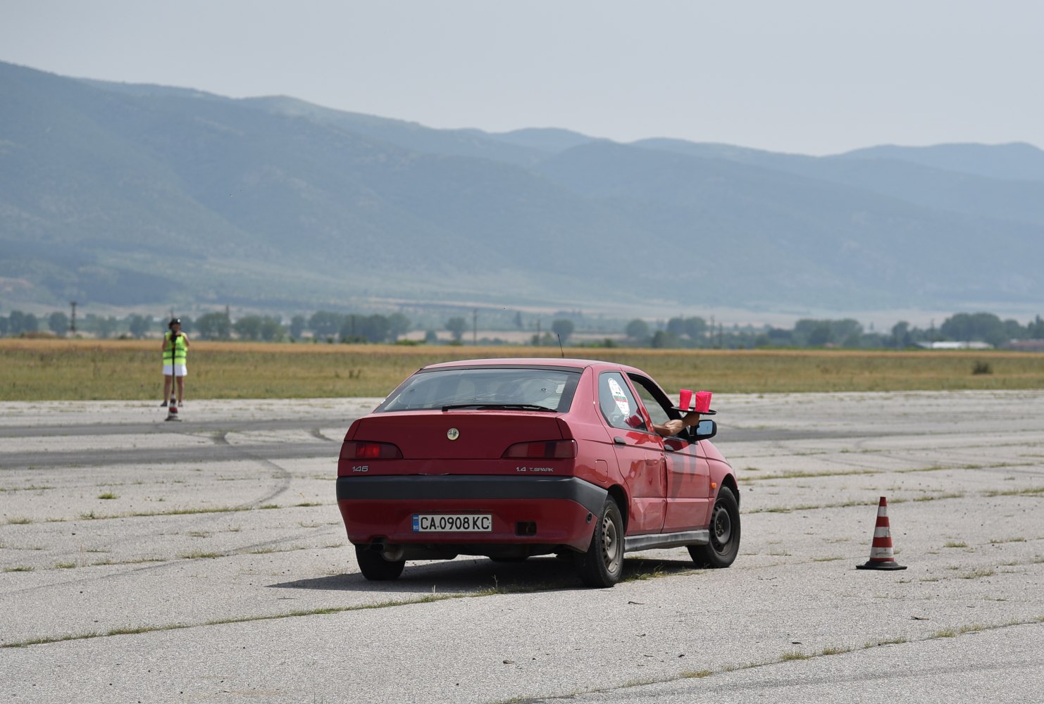 Rear view of red hatchback with hand holding cups outside window.