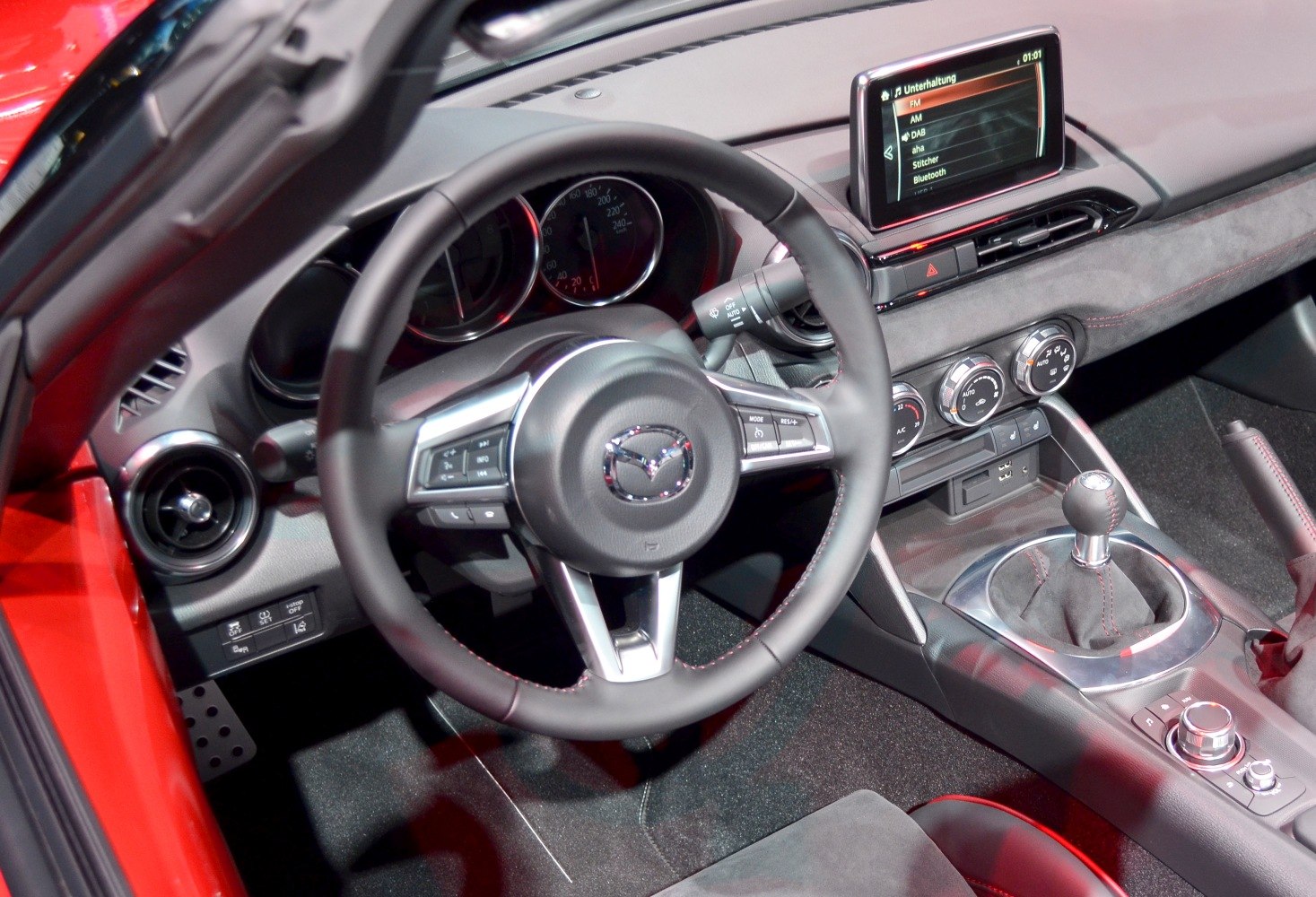 Mazda MX-5 IV interior showing steering wheel, manual gear shift, and infotainment screen