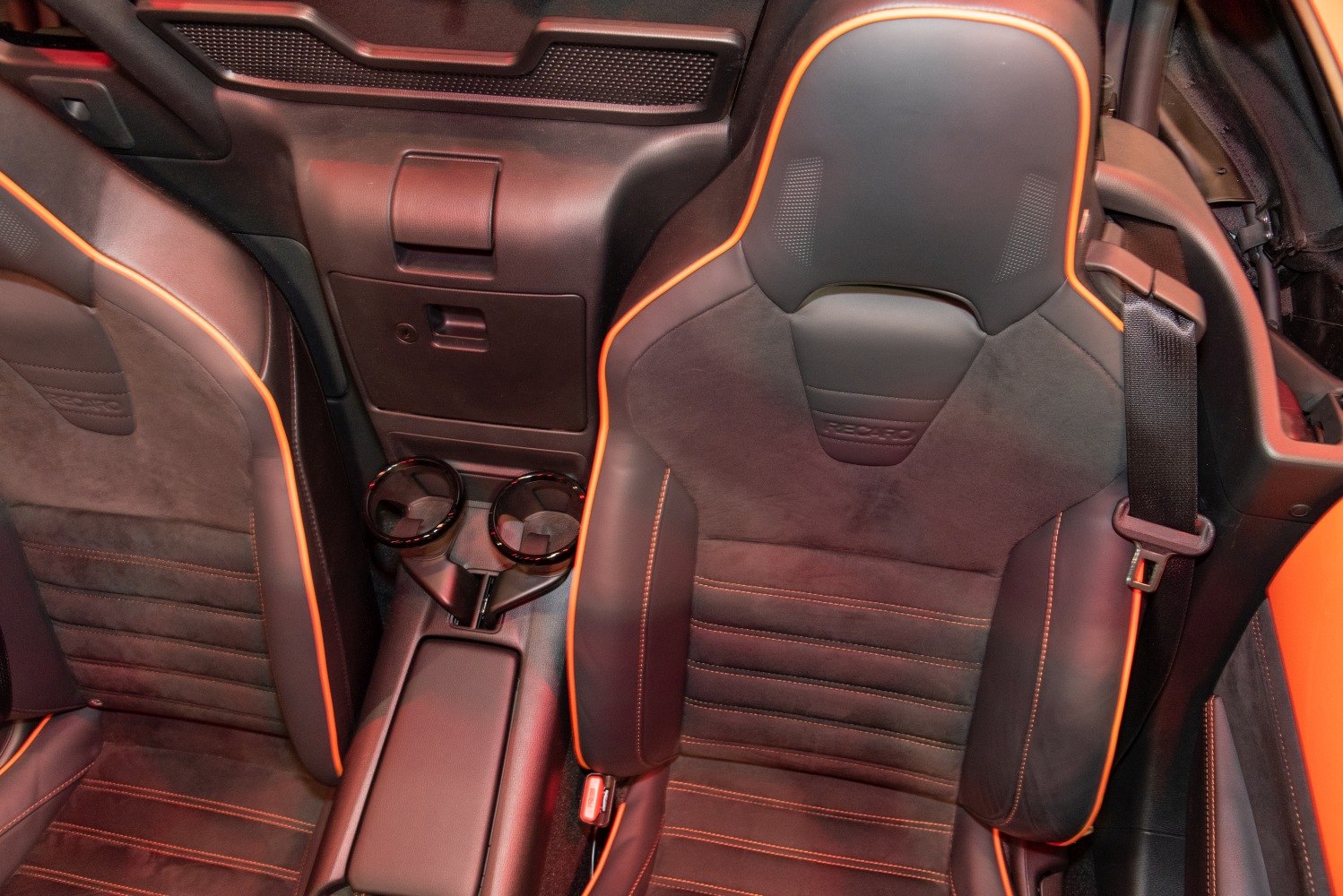 Recaro sport seats with orange piping and central cup holders.
