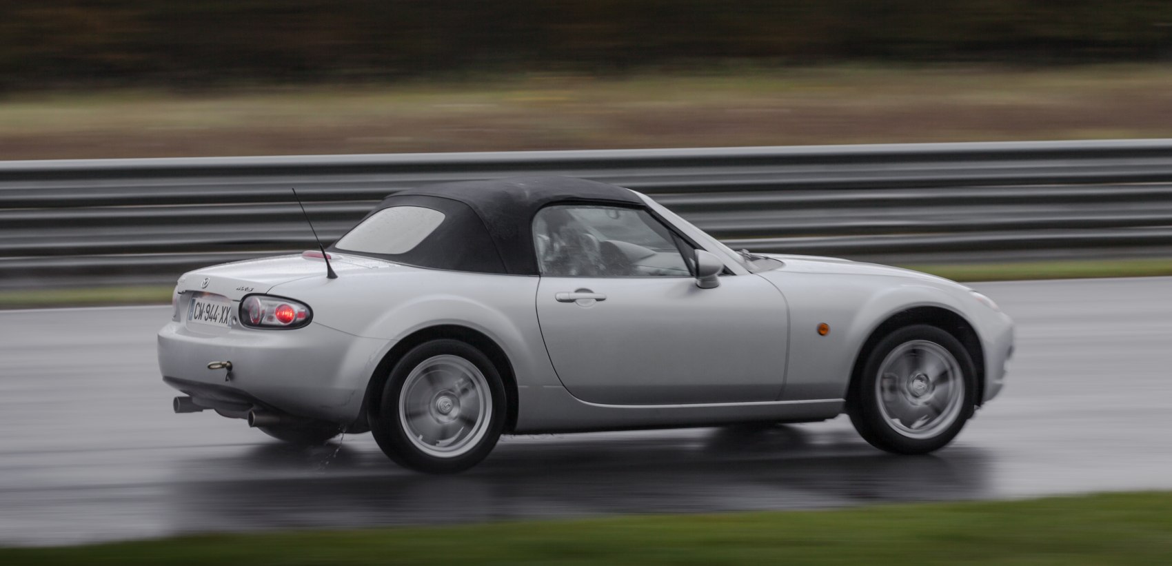Silver soft top convertible roadster in motion with rear side view