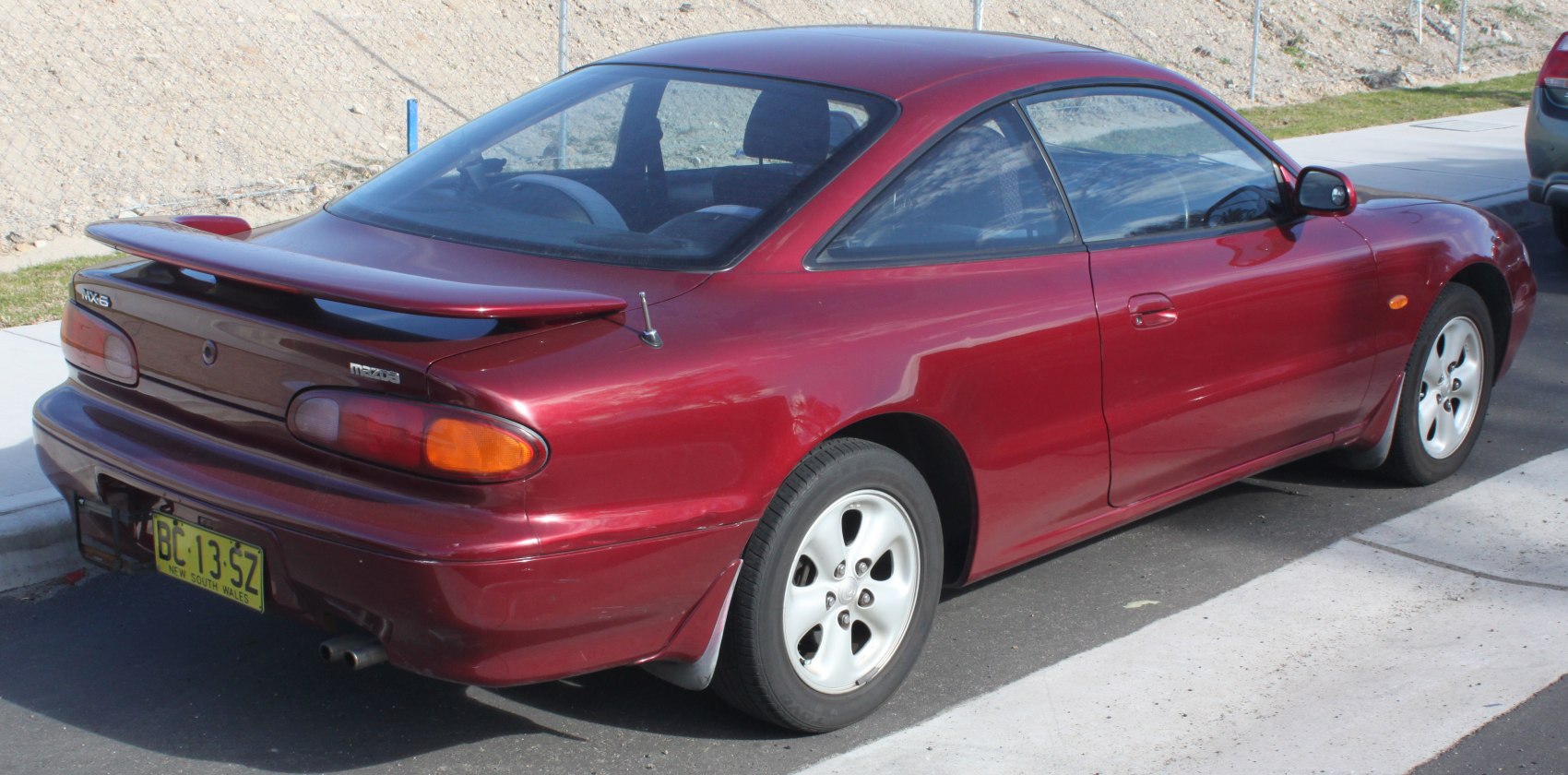 Rear side of red coupe featuring spoiler and distinct taillights