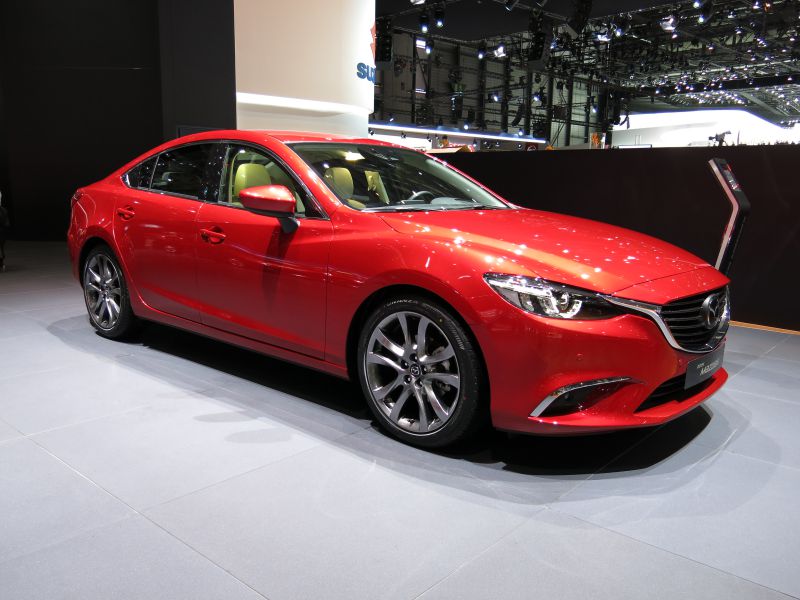 Red sedan with sleek front and side design and alloy wheels.