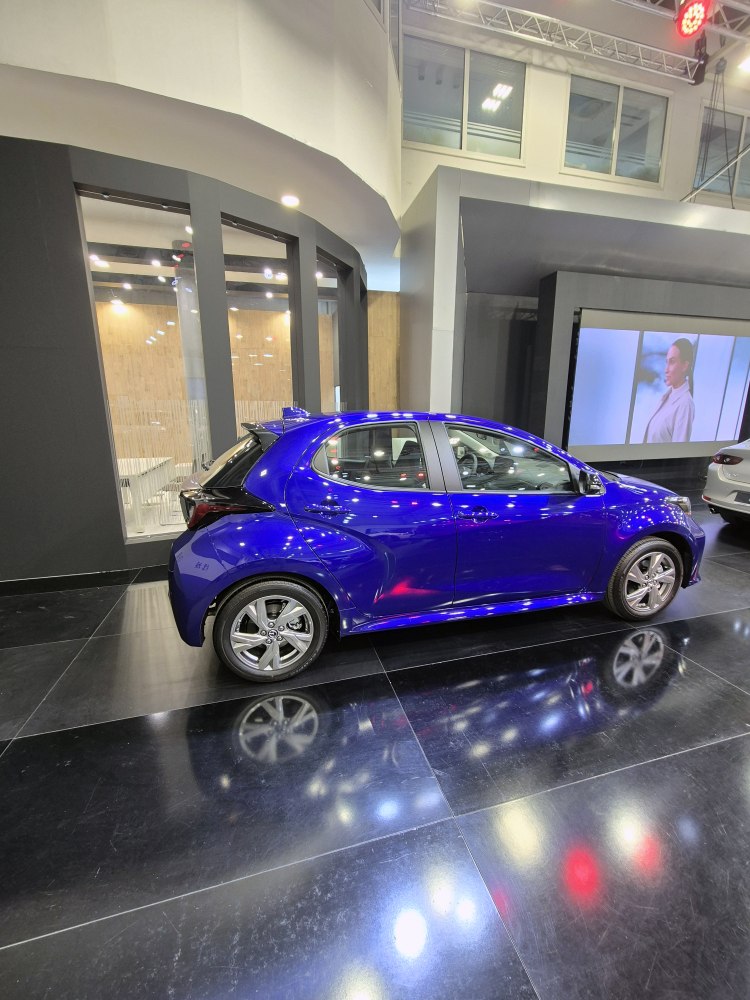 Side profile of a blue hatchback with alloy wheels in showroom