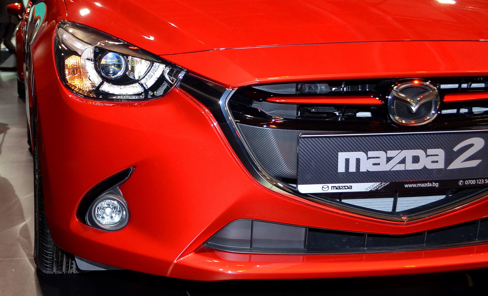 Close-up of front headlight, grille, and fog light of red car