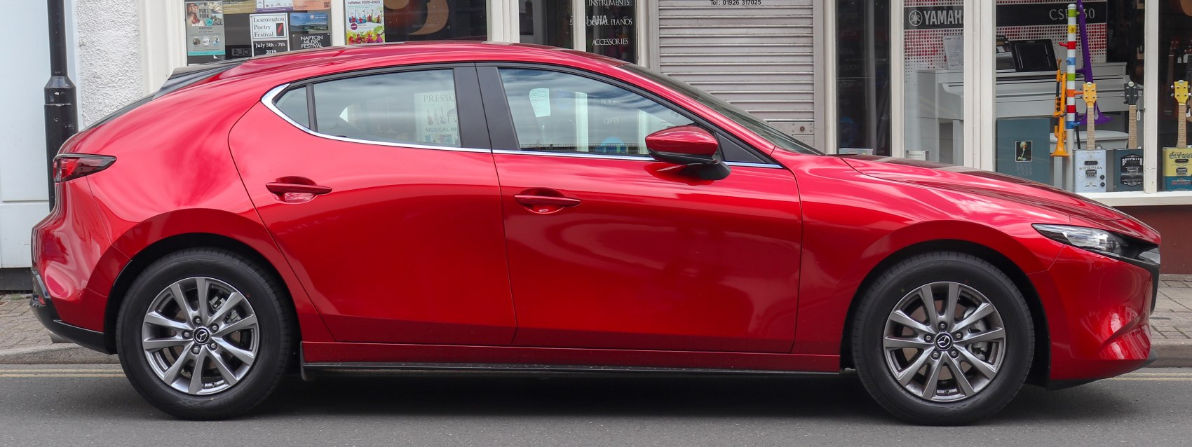 Side profile of a red hatchback with alloy wheels and smooth design lines