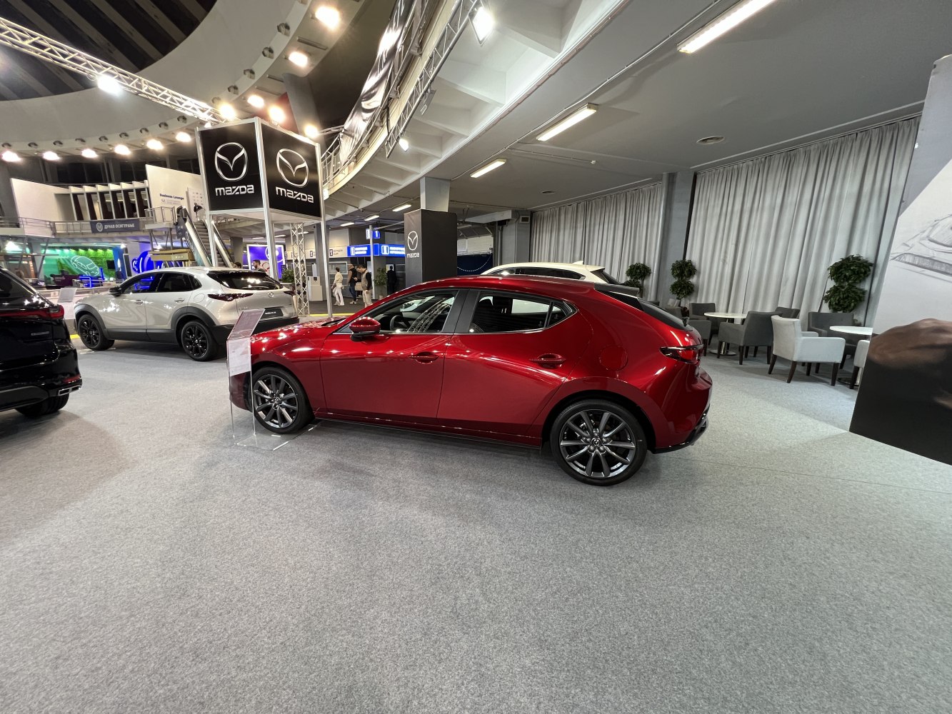 Red 5-door hatchback side profile with alloy wheels at indoor exhibit
