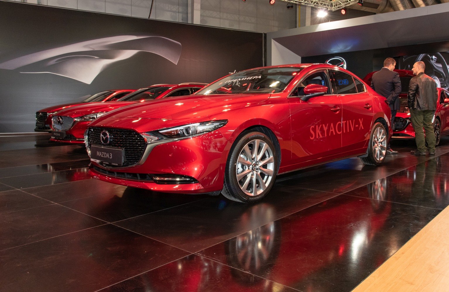 Red sedan with Skyactiv-X lettering and alloy wheels under showroom lighting