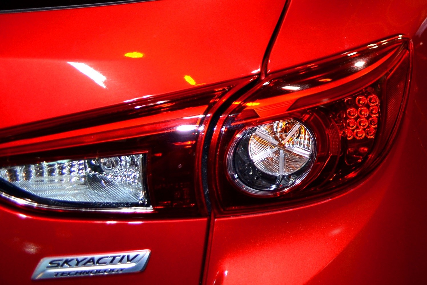 Close-up of modern rear taillight and Skyactiv badge on red hatchback.