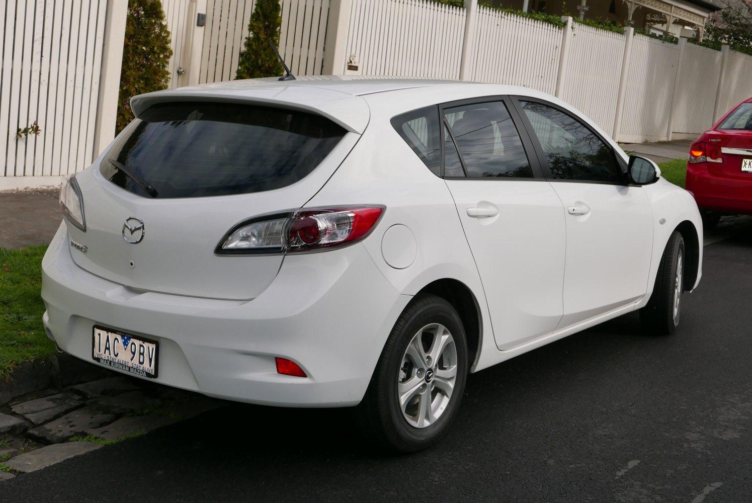 Rear side view of white compact hatchback with alloy wheels and spoiler