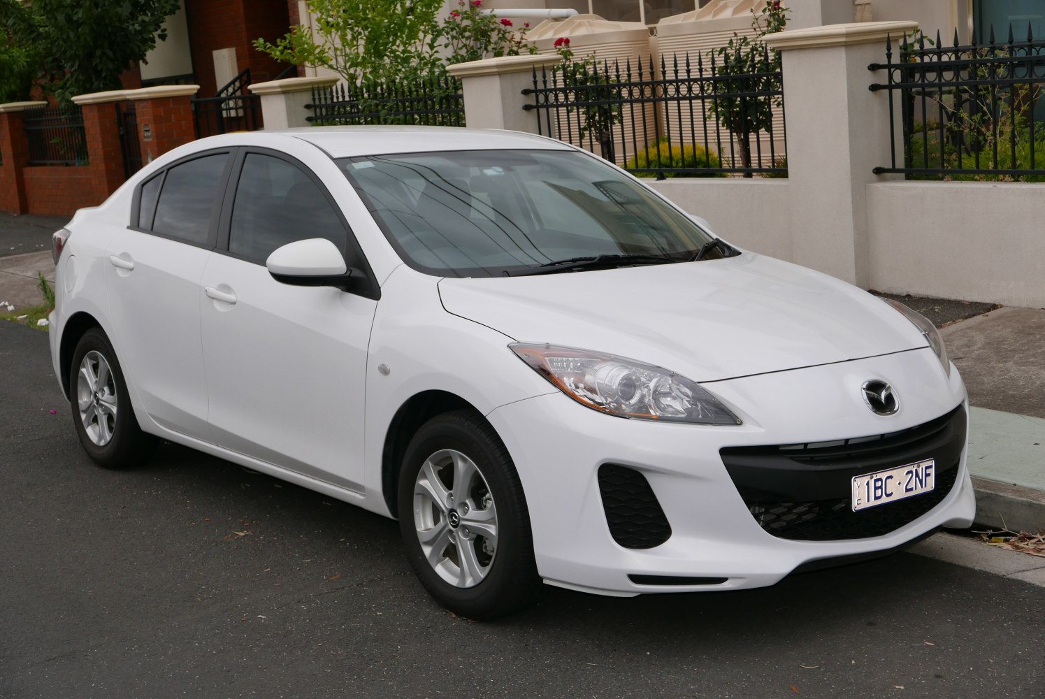 Front side view, white compact sedan with alloy wheels and chrome headlight
