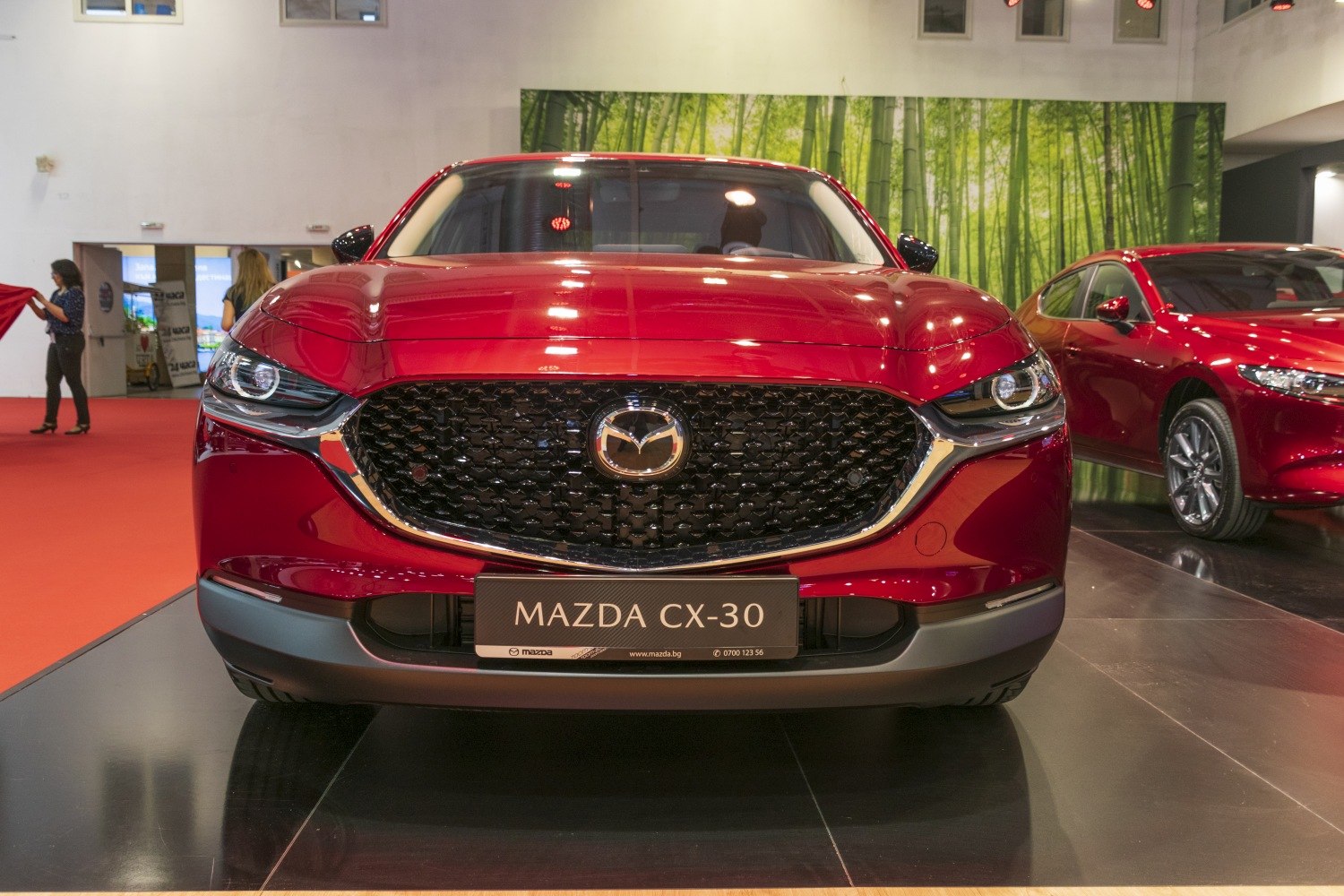 Large black grille with chrome outline and sleek LED headlights on a shiny red car front.