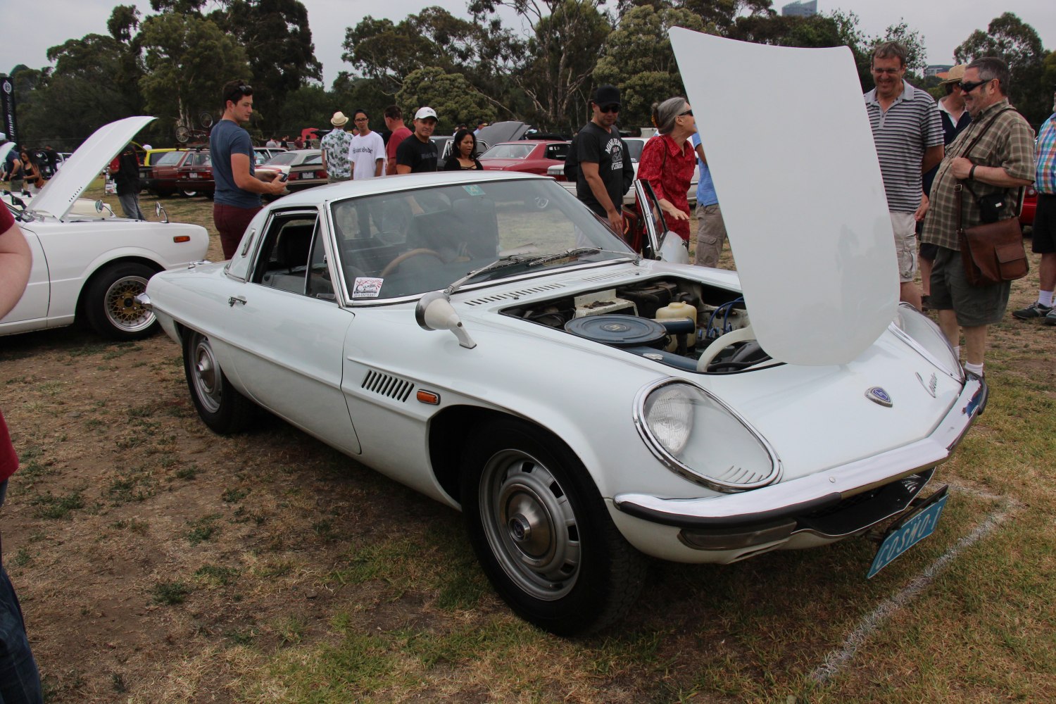 White classic coupe with open hood showing engine at a car gathering
