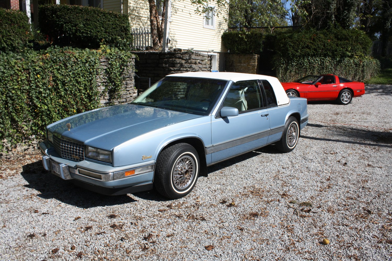 Wire-spoke wheels and white vinyl roof on a light blue classic coupe