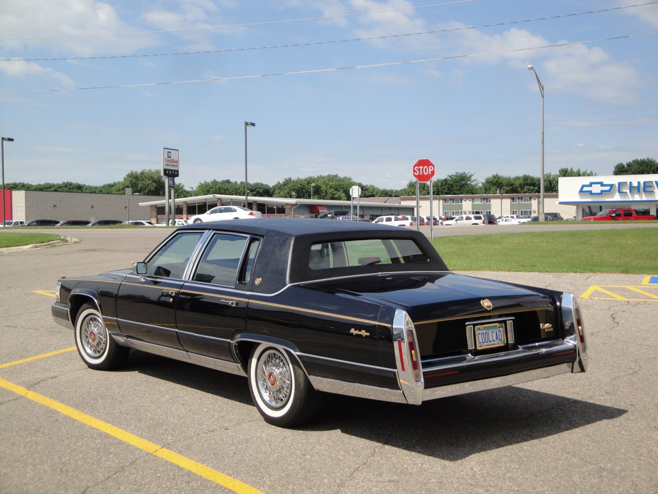 Rear and side view of a black luxury sedan with vinyl roof and wire spoke wheels.