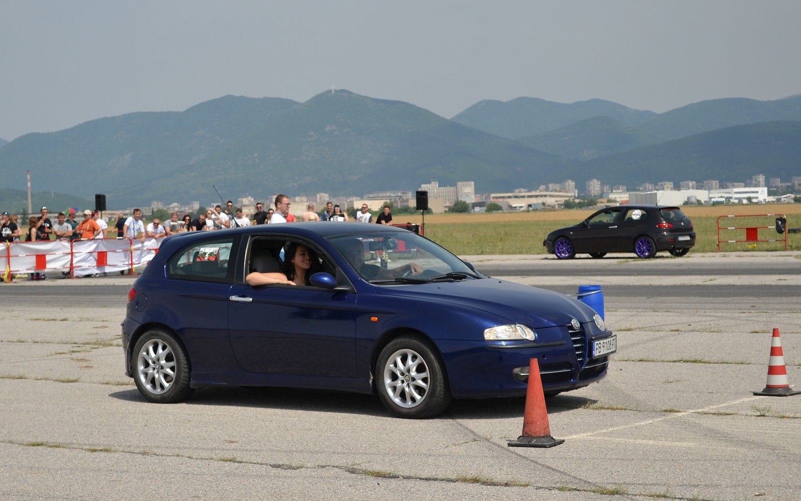 Blue 3-door hatchback navigating orange traffic cones on asphalt track.