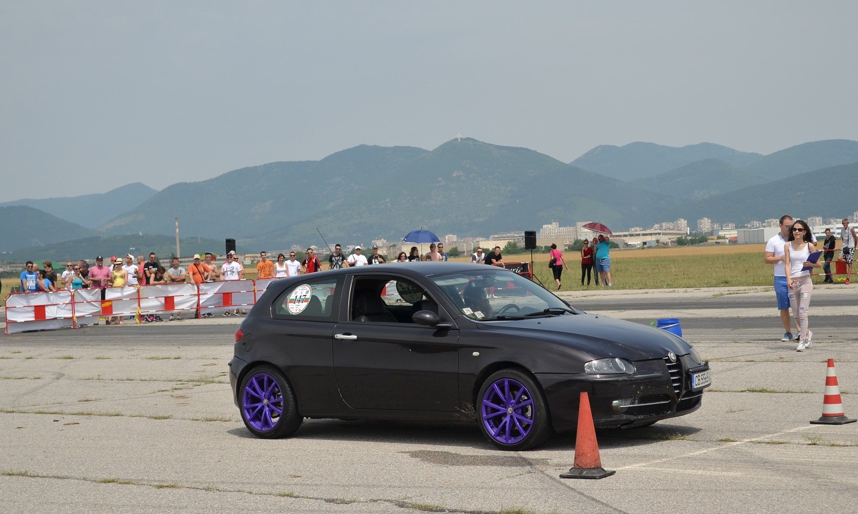 Black 3-door hatchback with purple rims at a motorsport event