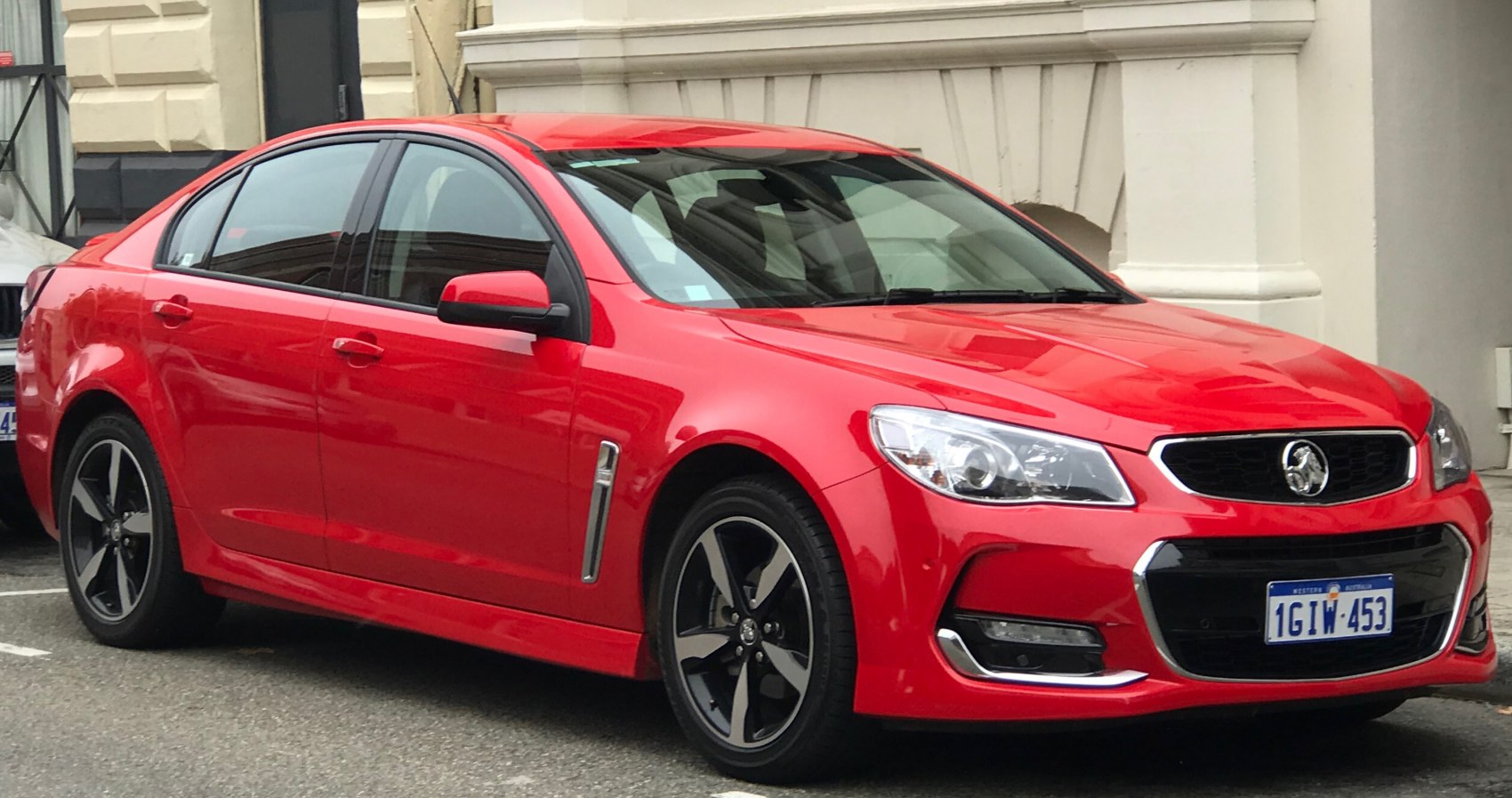 Red sedan with modern alloy wheels and chrome accents, front side view