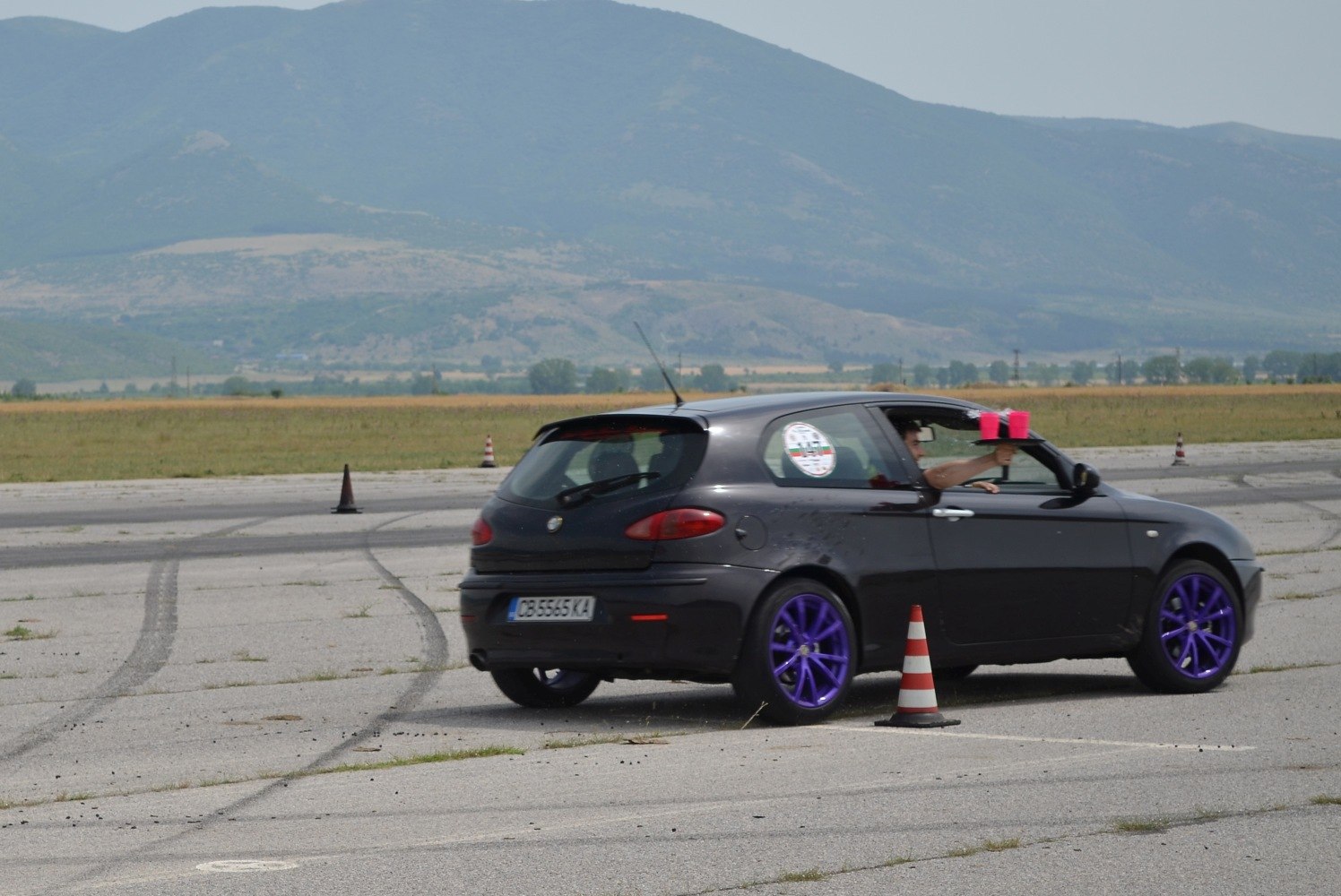 Black compact hatchback with vibrant purple alloy wheels driving on open track