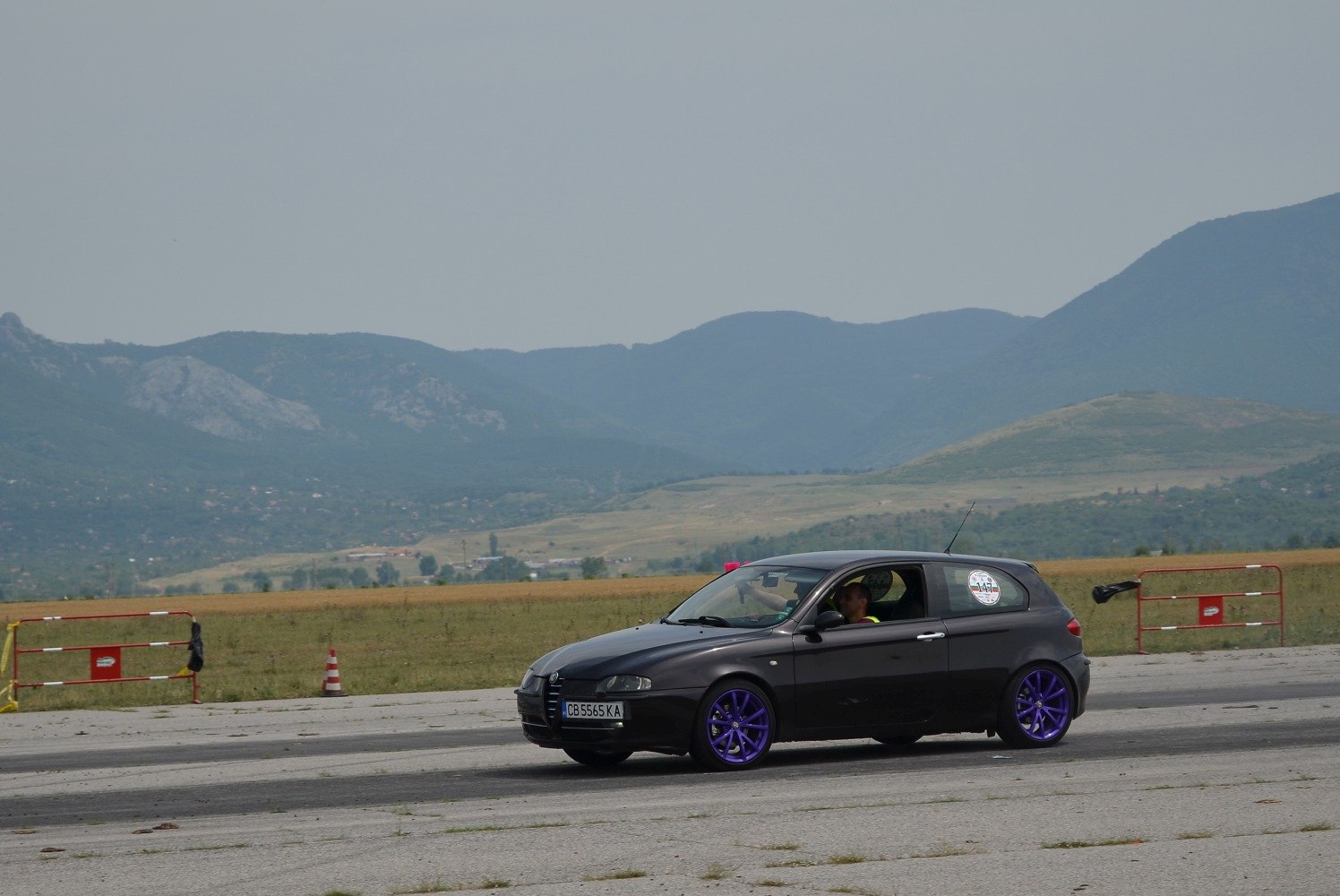 Black hatchback with signature purple wheels on a race track.