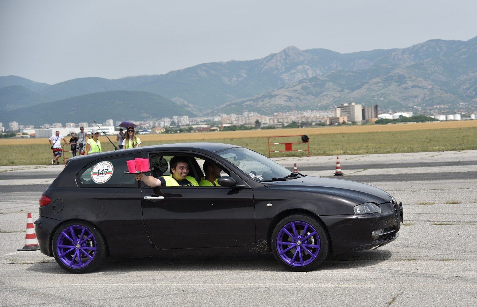 Black 3-door hatchback with purple alloy wheels on open tarmac