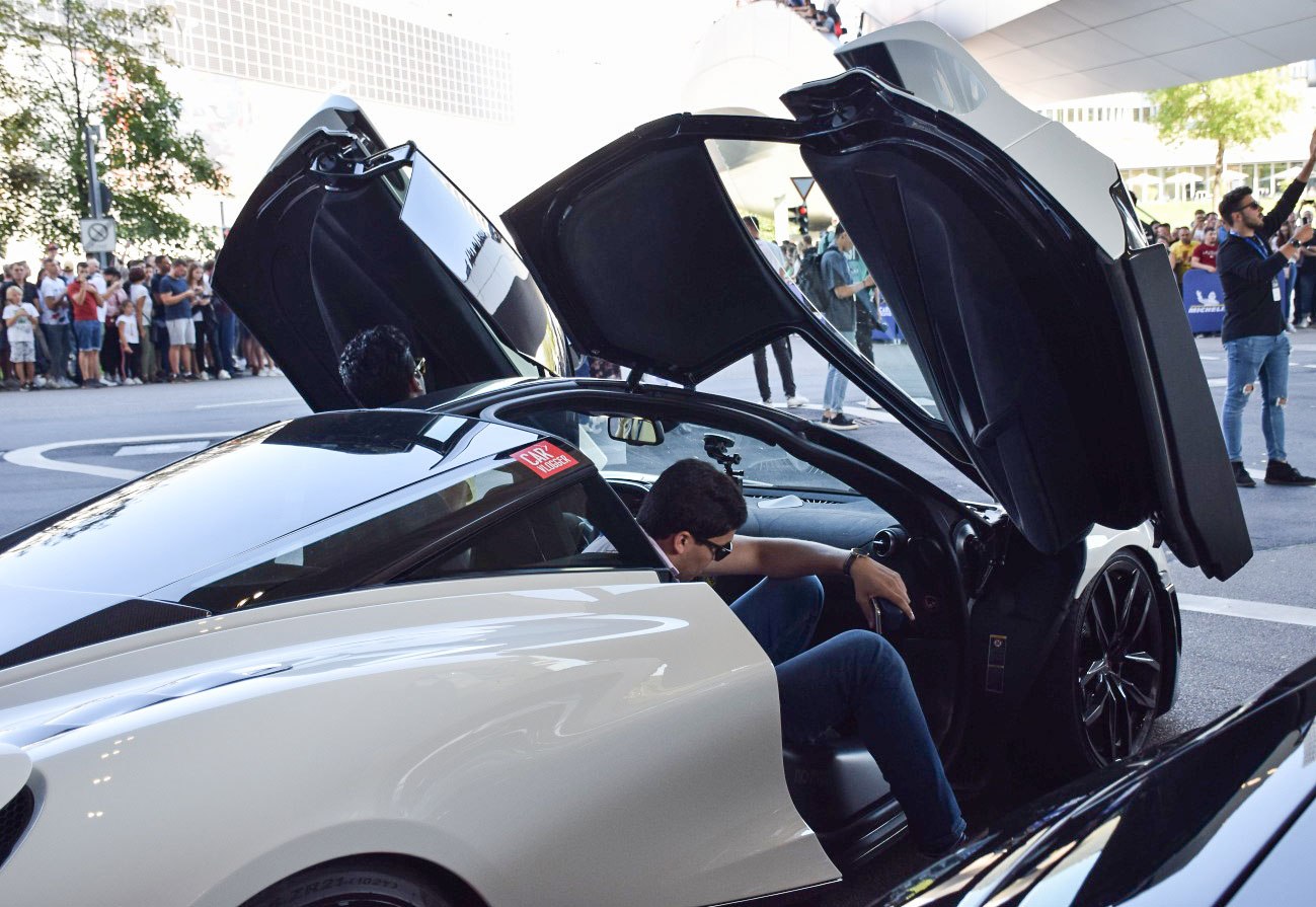 Butterfly doors open on a sleek sports car with driver entering.