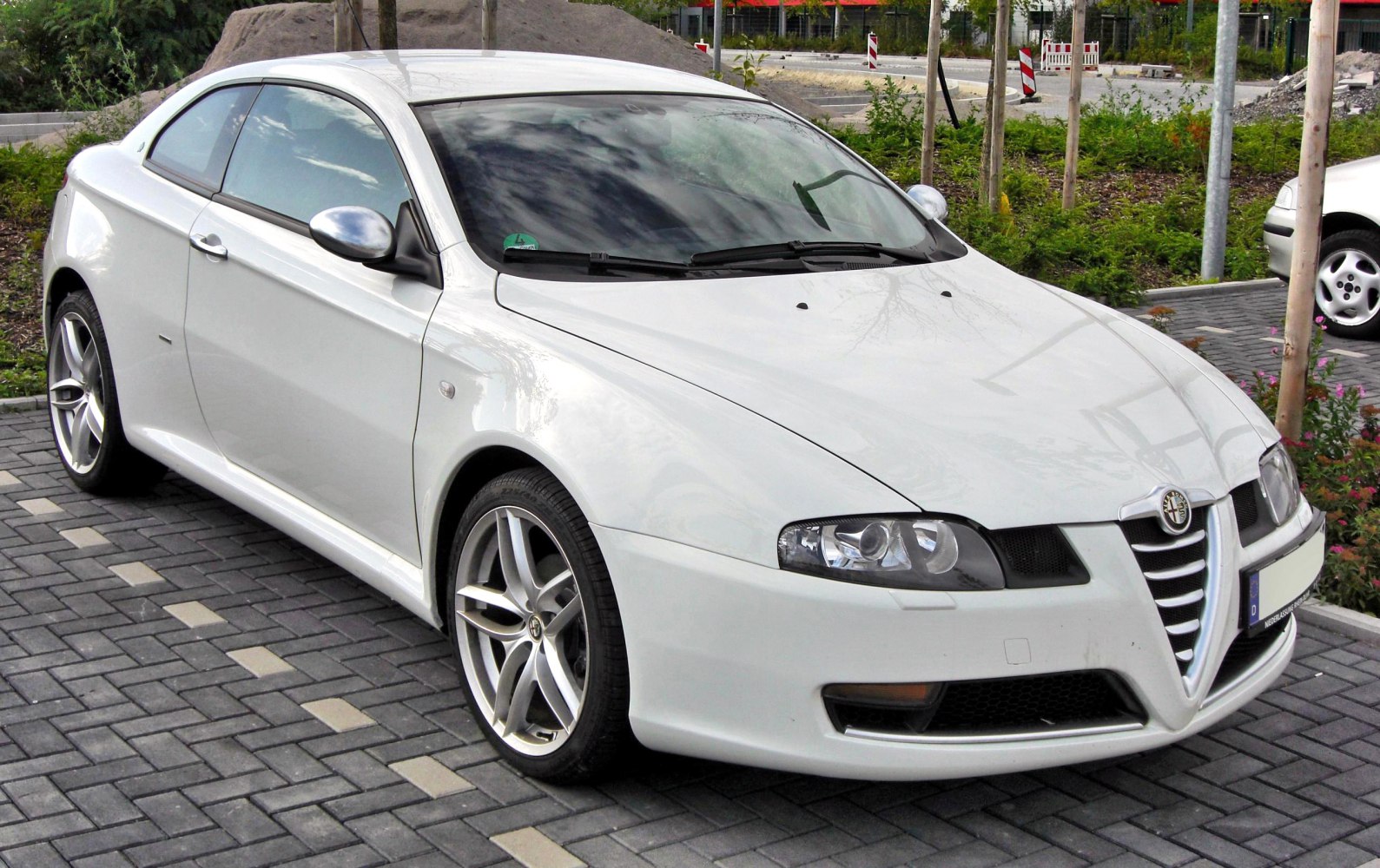 White coupe with distinct Alfa Romeo grille and sporty alloy wheels.