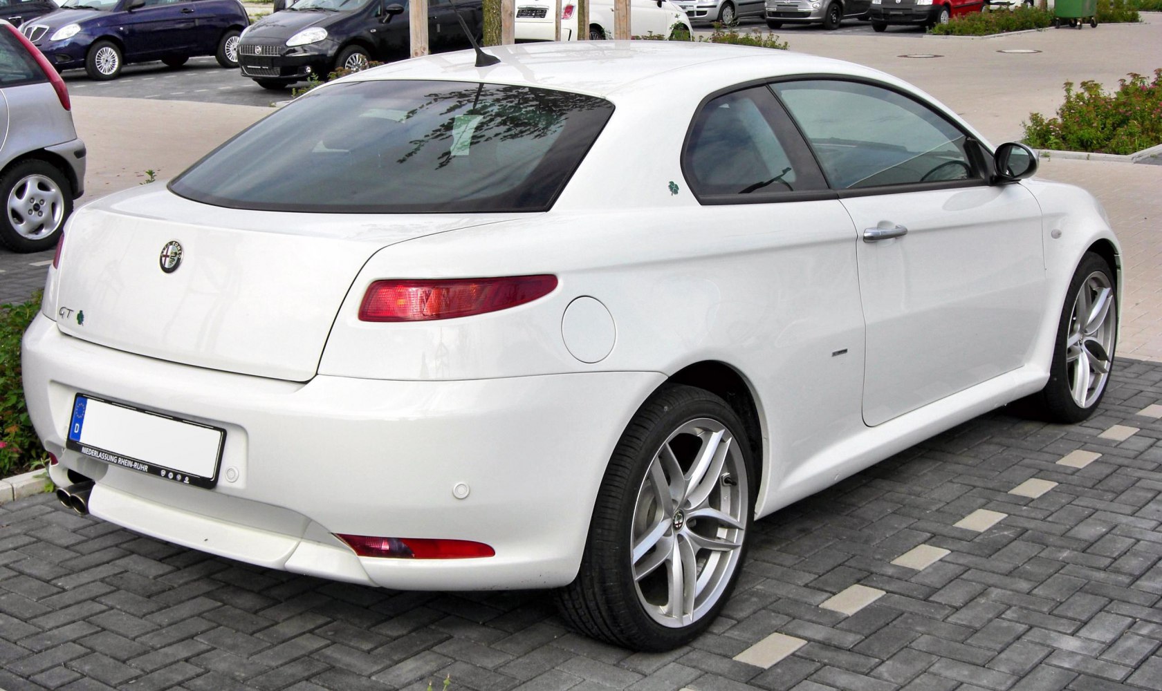 Rear view of white coupe with sporty alloy wheels and dual exhaust