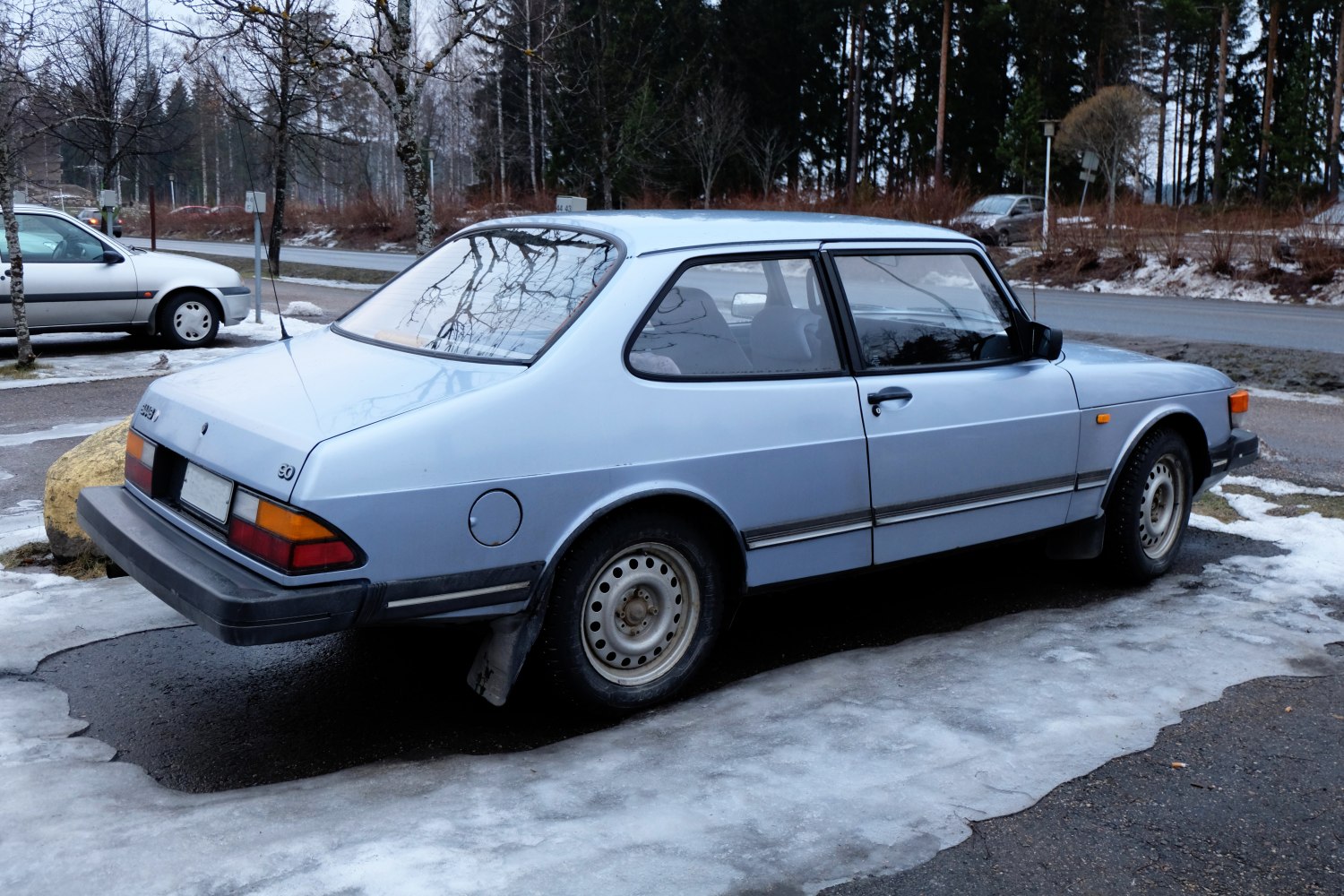 Rear side view of a vintage coupe with smooth lines and distinct taillights on icy pavement