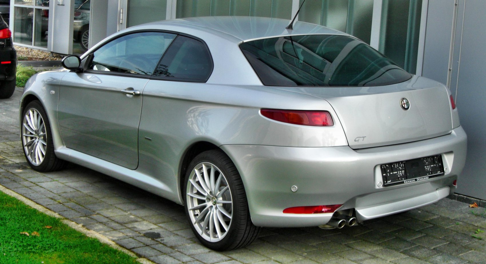 Silver compact coupe rear side with twin exhaust and multi-spoke wheels