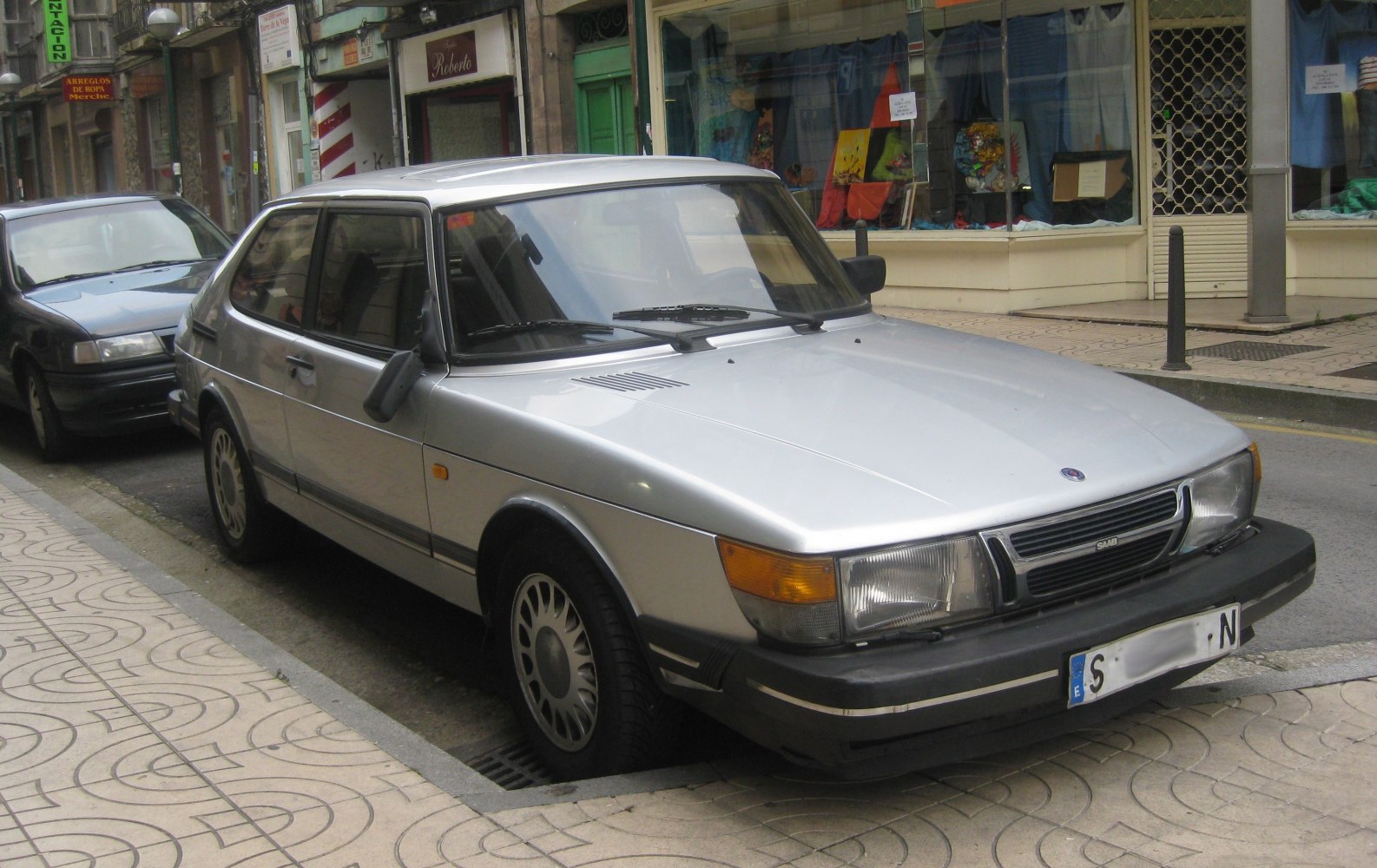 Urban street view of a silver vintage hatchback with angular front-side design