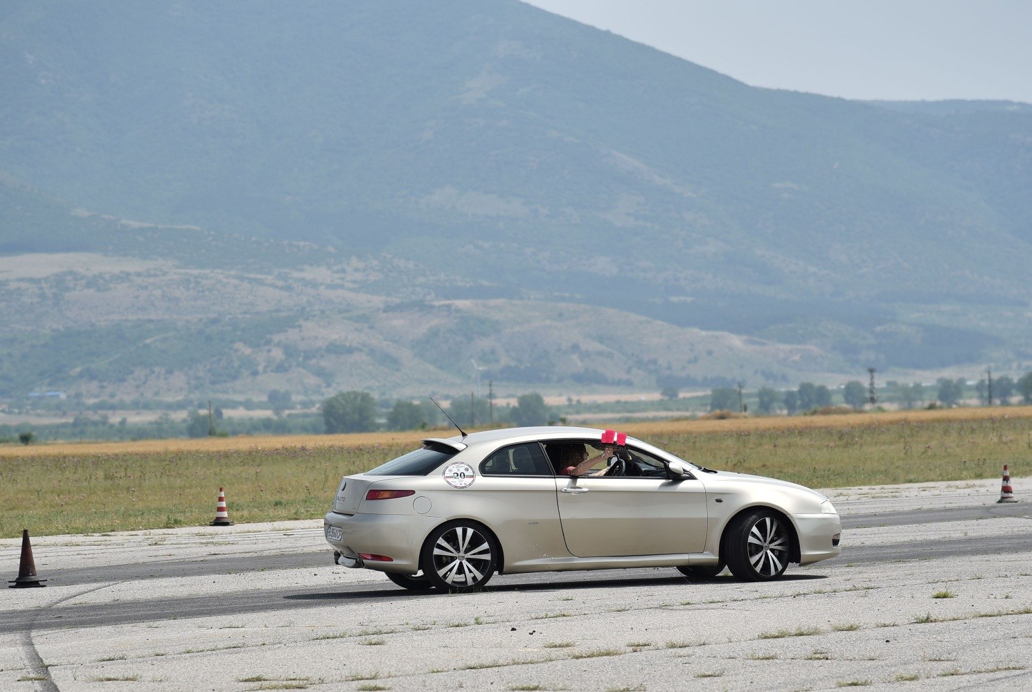 Silver two-door coupe on open pavement with mountains and traffic cones