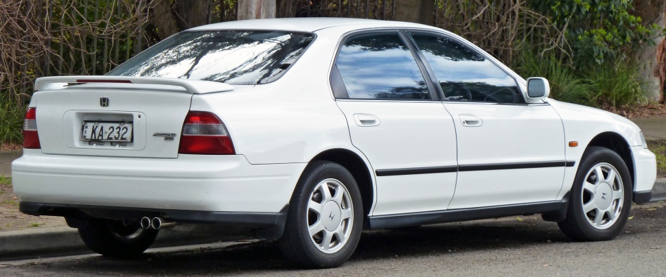 Rear side view of white sedan with rear spoiler and stock wheels.