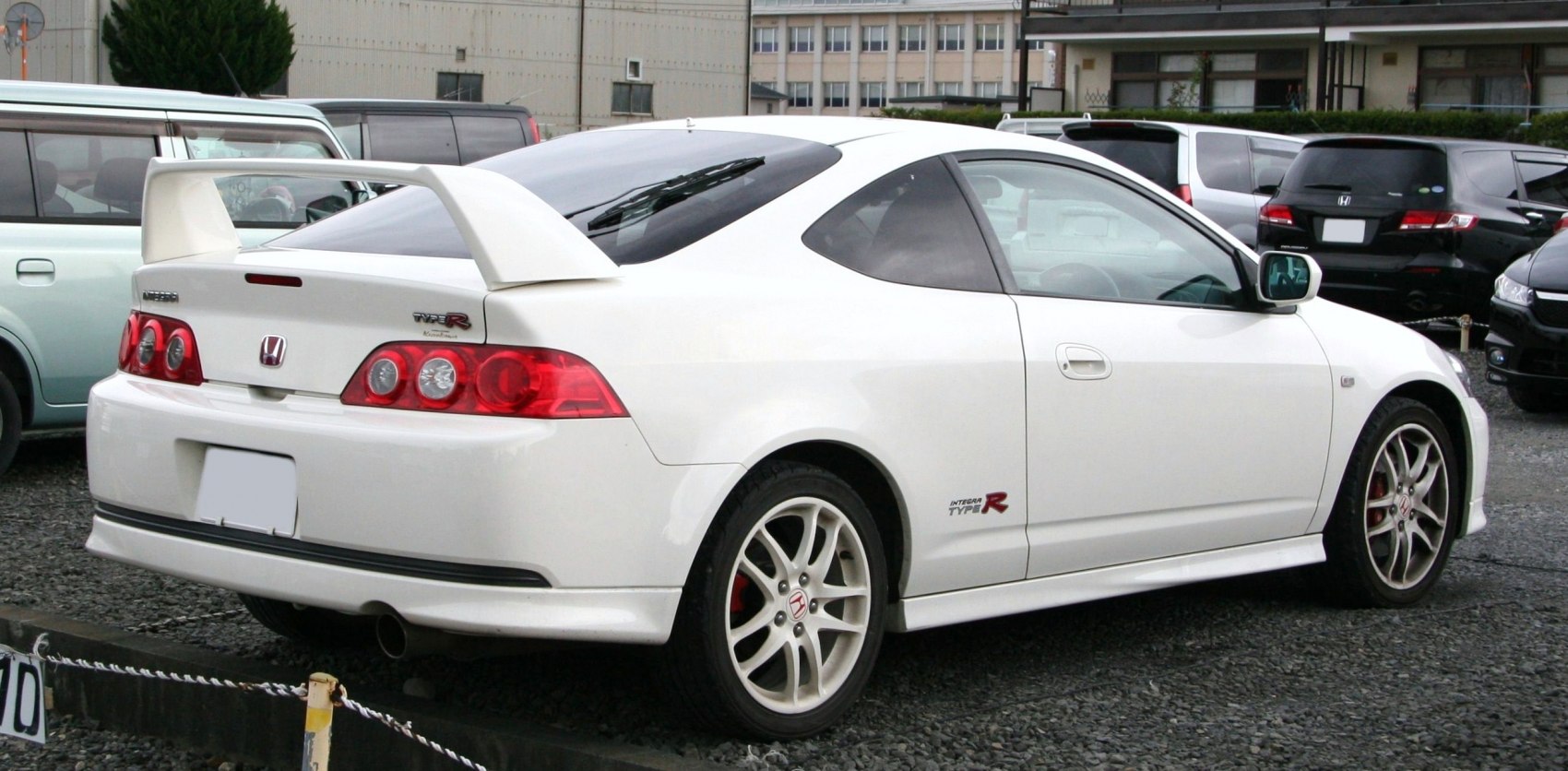 Rear-side view of a white sports coupe with large rear spoiler and alloy wheels
