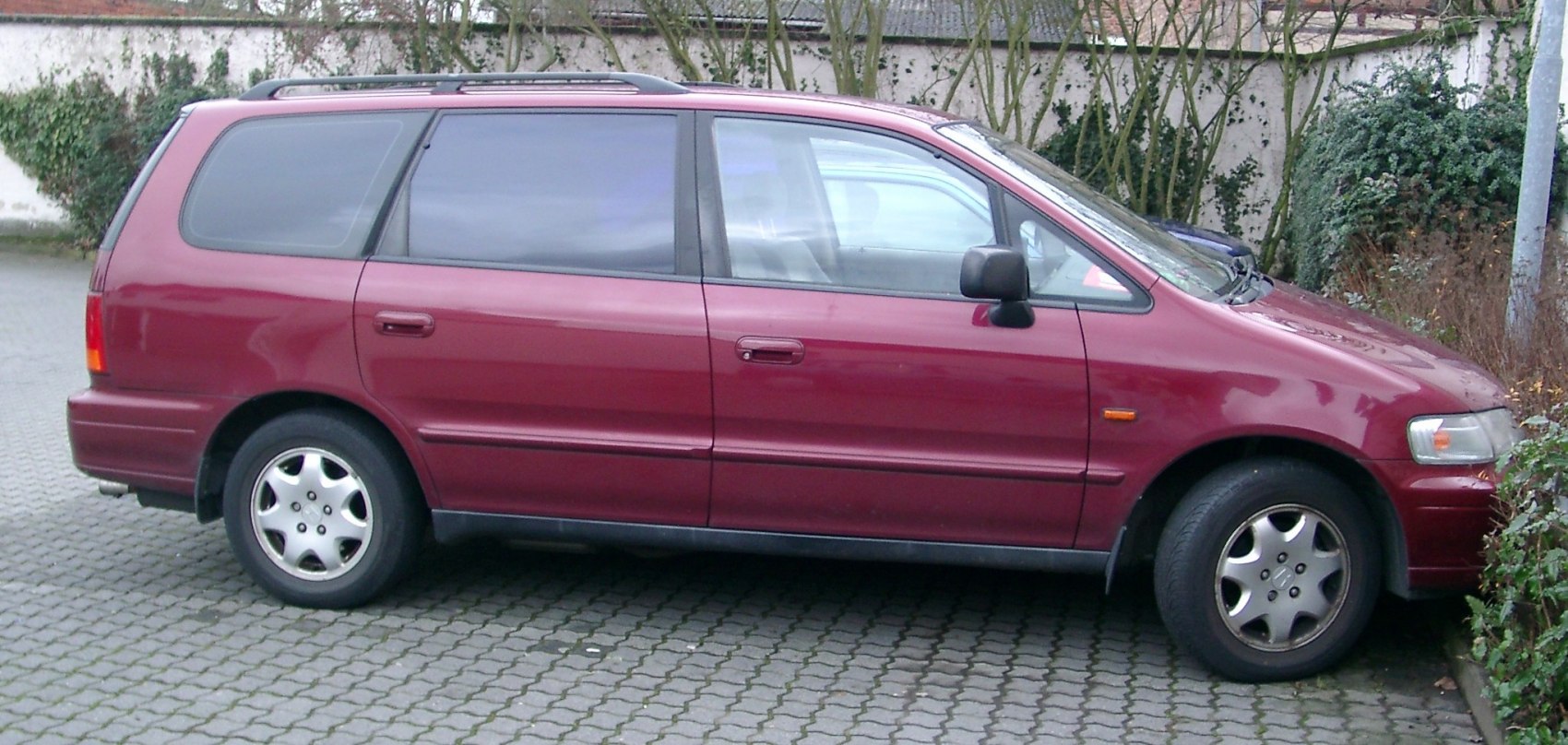 Side profile of red minivan with roof rails and alloy wheels