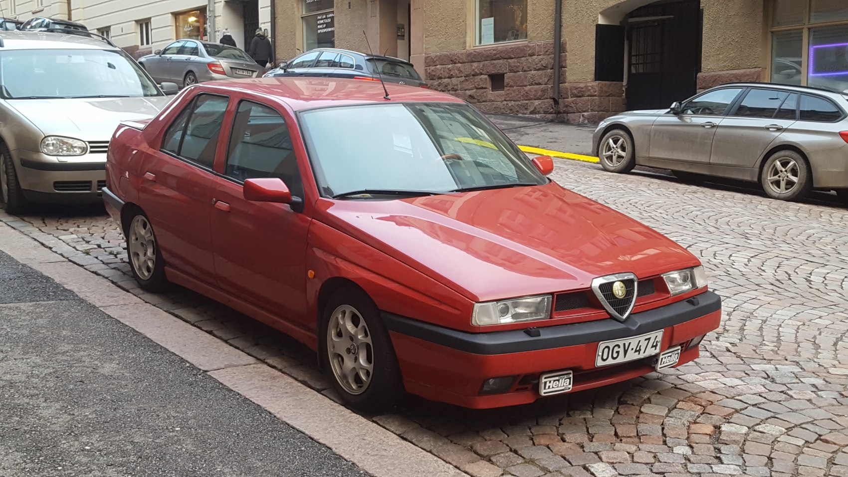 Sharp front grille and rectangular headlights with Hella fog lights on a red sedan.
