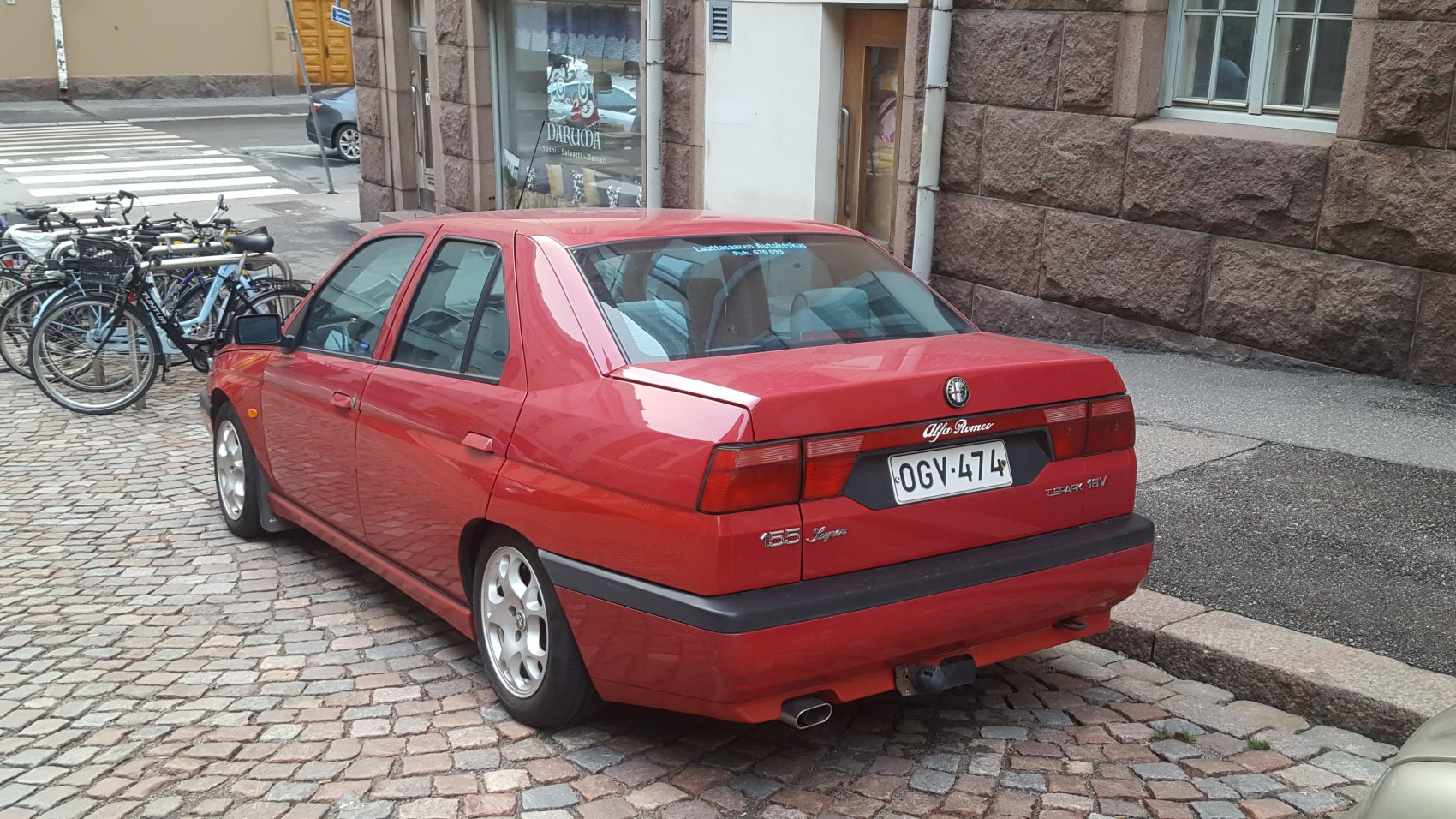 Red sedan rear view with Alfa Romeo badge and taillights on cobblestone urban street