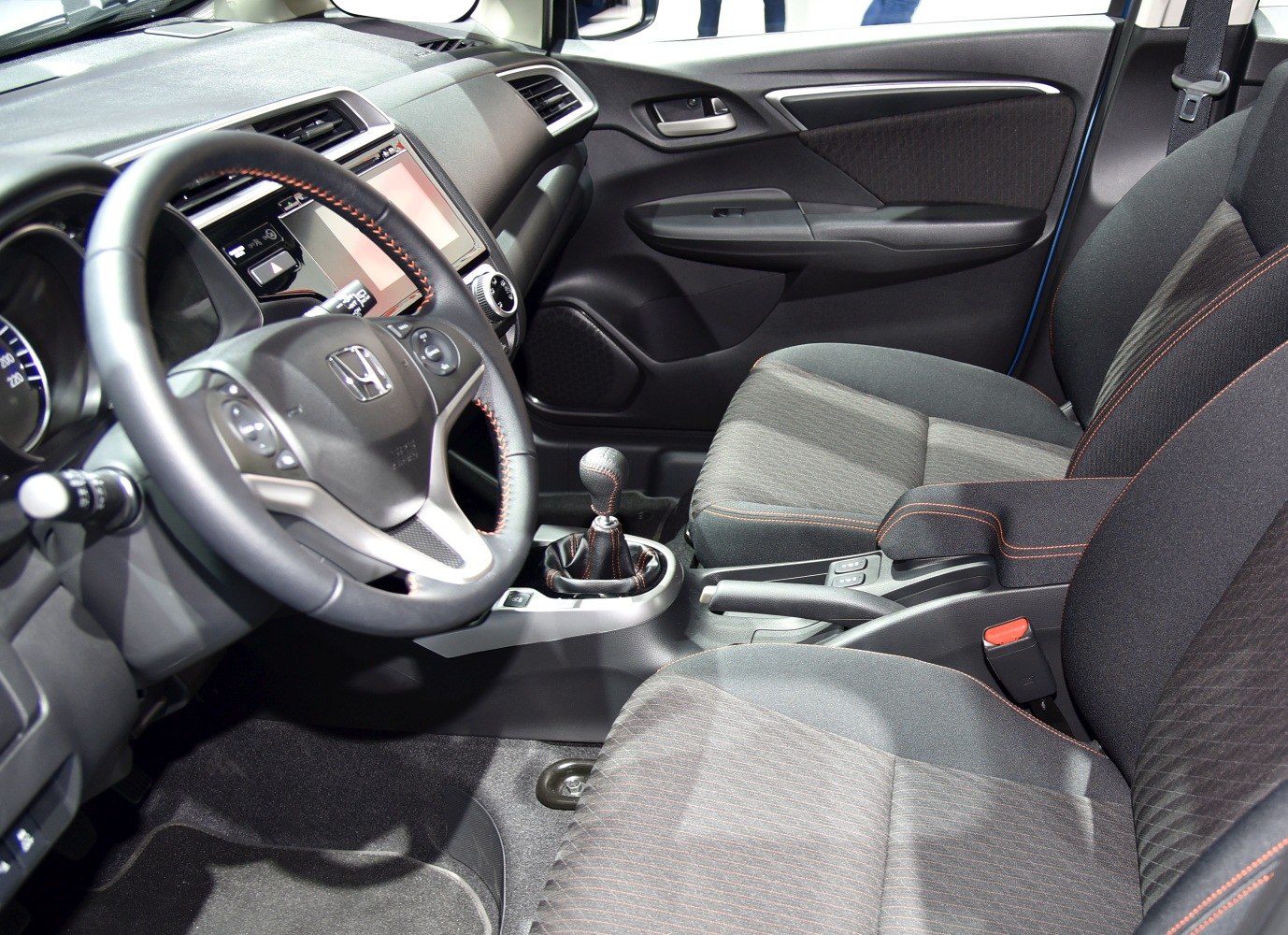 Steering wheel, manual gear stick, and fabric upholstery inside a compact car.