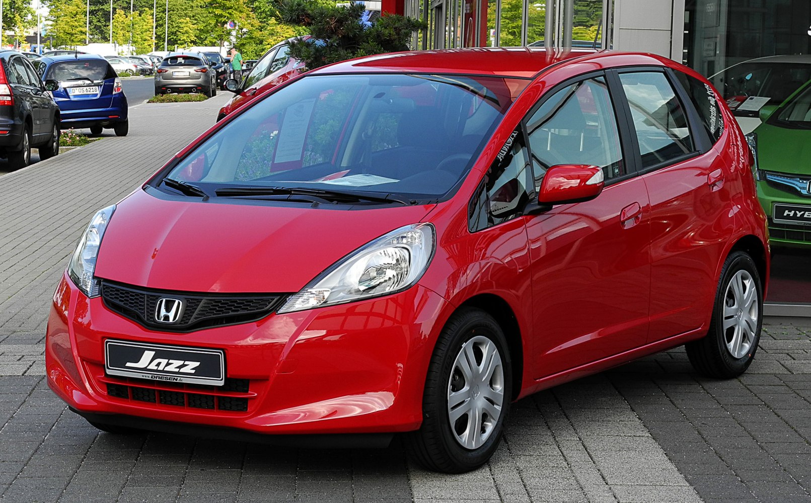 Red compact hatchback front three-quarter view with headlights and grille.