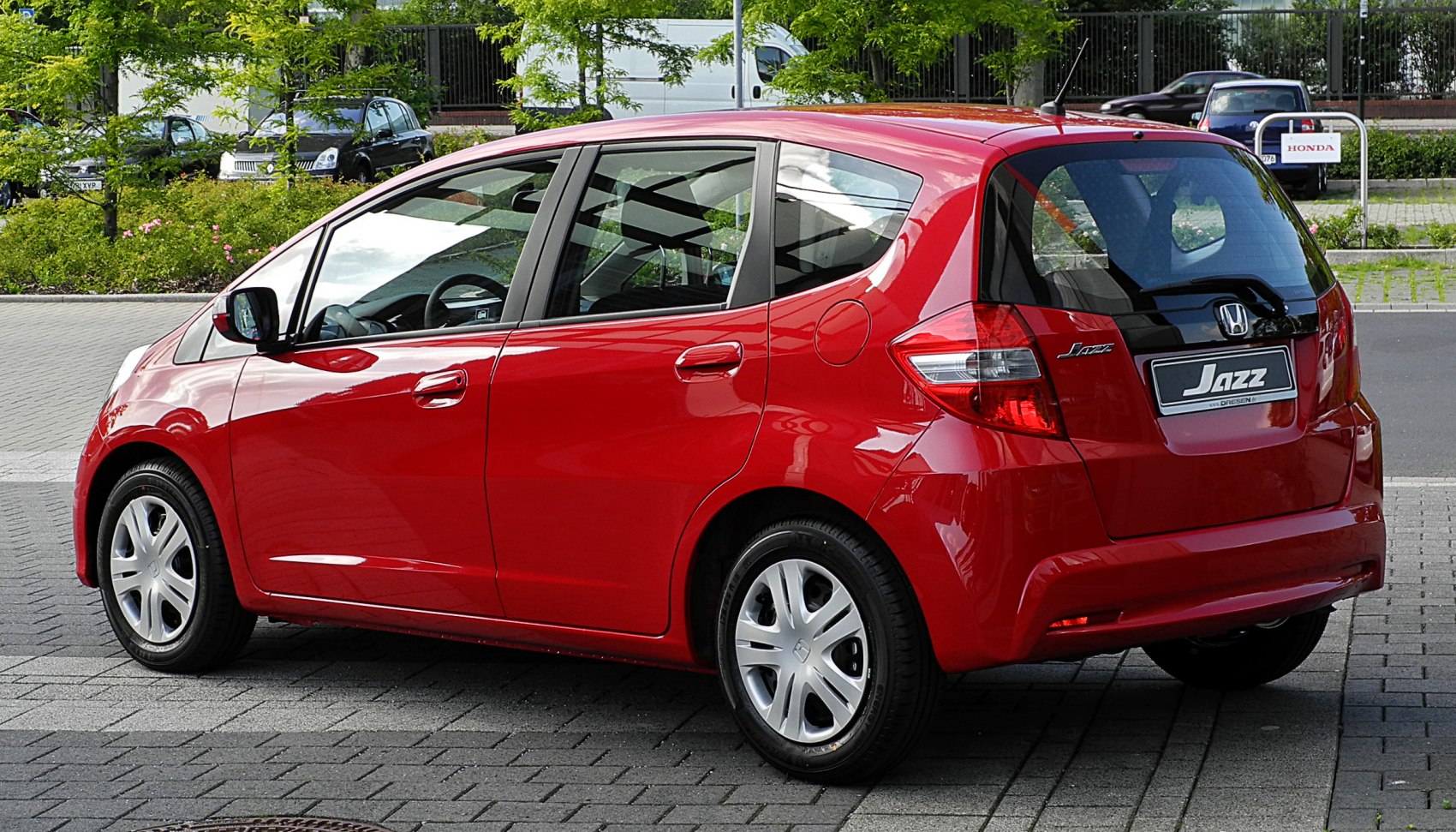 Rear and side view of red compact hatchback with distinctive window design.