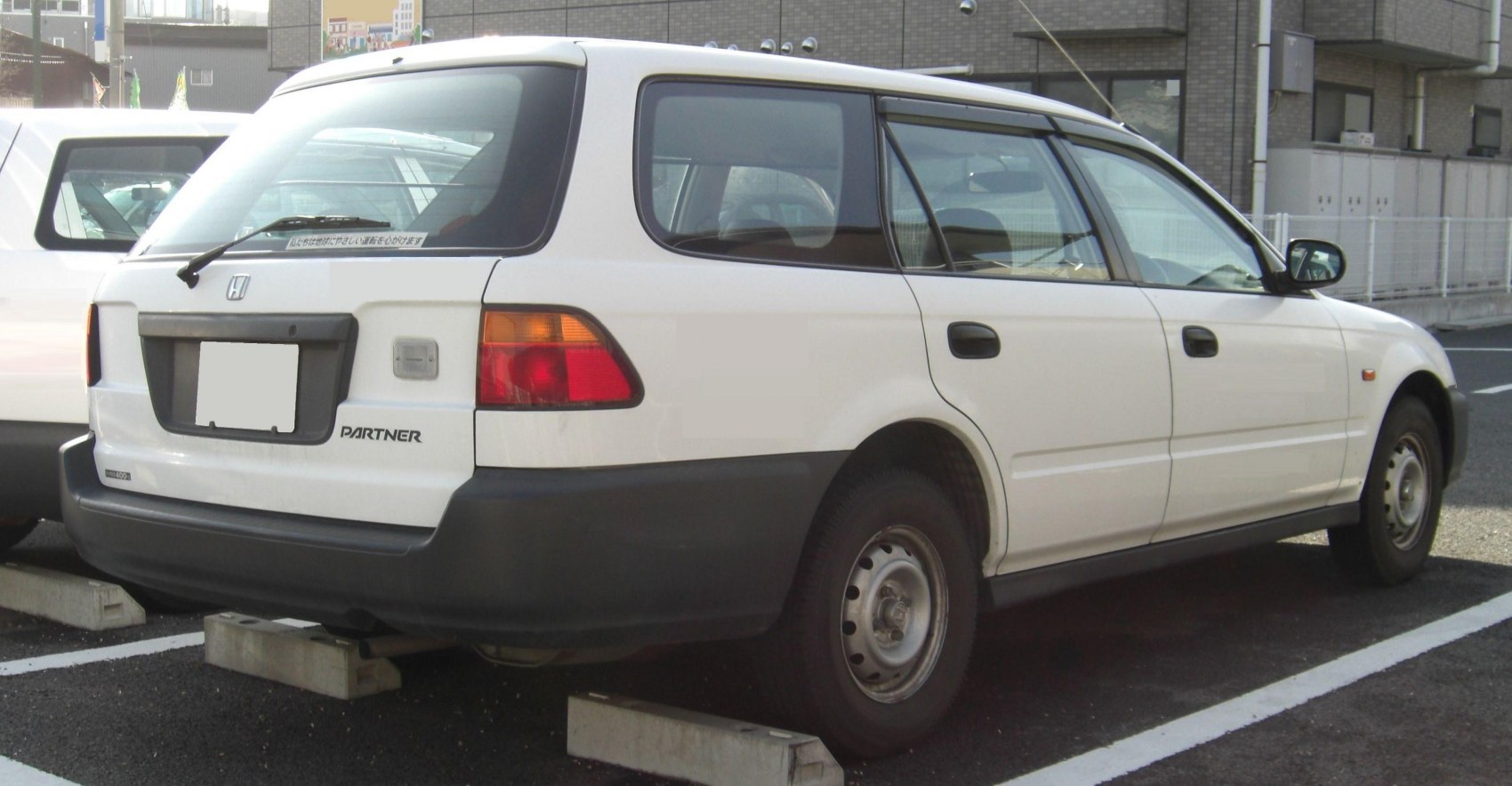 Rear and side view of a white station wagon with black bumpers and steel wheels.
