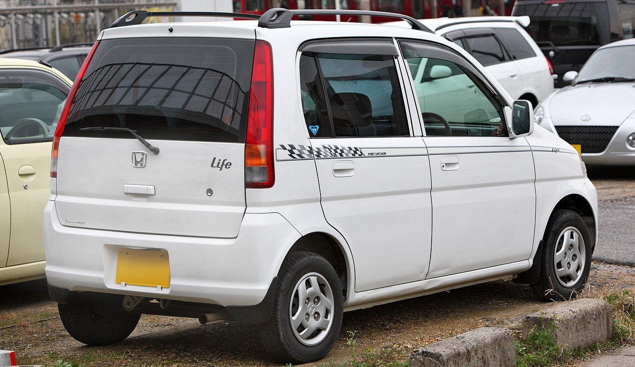Rear-side view of compact white hatchback with roof rack and checkered decal