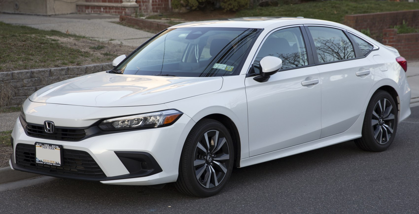 Front and side exterior view of a white sedan with modern headlights and alloy wheels