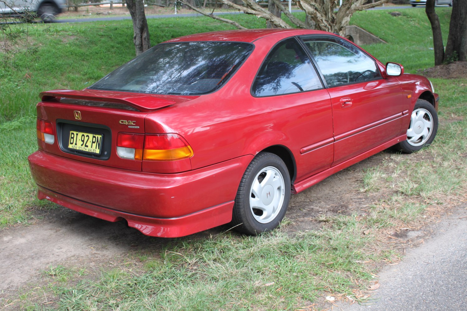 Rear view of red coupe with spoiler and classic wheel covers