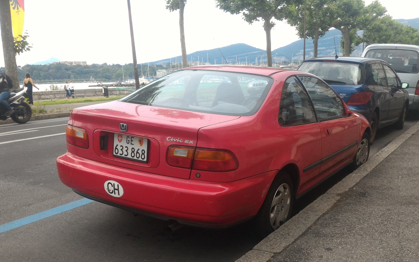 Rear view of a red coupe parked beside curb in city setting