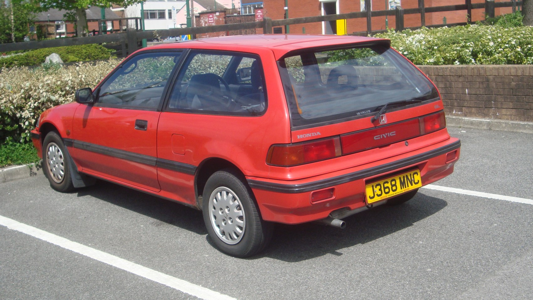 Rear-side view of red hatchback with wide rear window and compact design