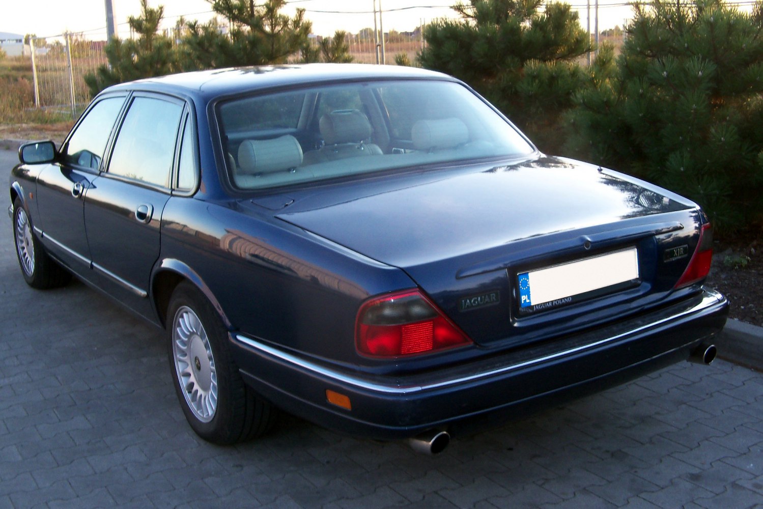 Rear view of a 1990s luxury sedan with classic tail lights and dual exhaust pipes.