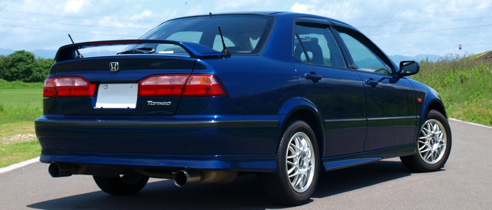 Rear view showing spoiler and dual exhaust of a blue sedan