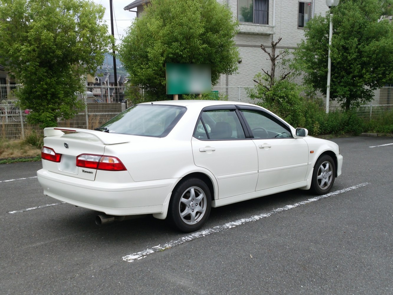 White sedan rear-side view with spoiler and alloy wheels