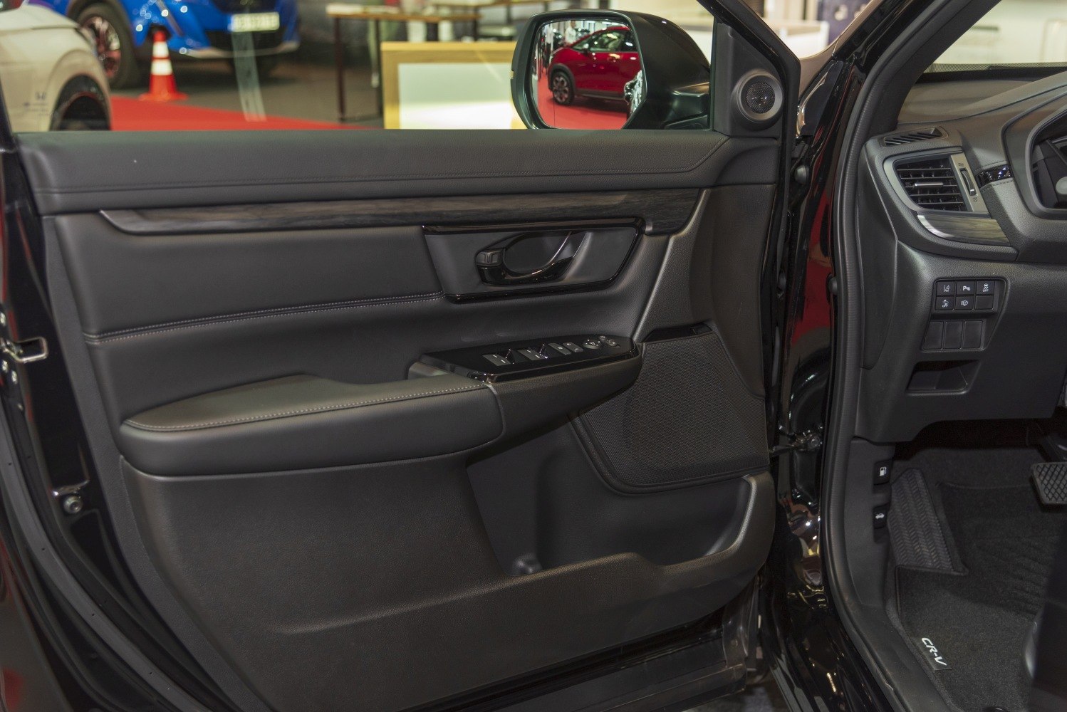 Car door interior panel with wood trim, control buttons, and speaker grille.